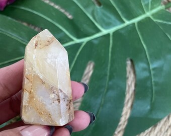 May include: A light brown and white crystal point with a pointed tip. The crystal is smooth and polished, with a translucent appearance.