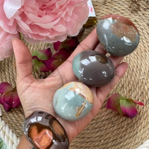 May include: Four smooth, polished, round stones with different patterns of brown, gray, and green colors. The stones are arranged in a hand, with the largest stone at the bottom.