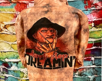 May include: A brown hooded sweatshirt with a bleach-splattered design. The front of the sweatshirt features a graphic of Freddy Krueger from the movie 'A Nightmare on Elm Street' with the text 'Don't Stop Dreamin'.