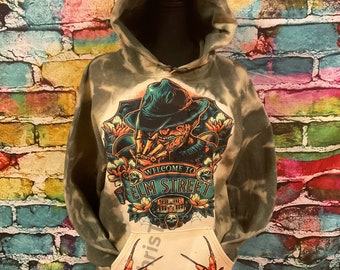 May include: A green and white tie-dye hoodie with a graphic print of Freddy Krueger from the movie "A Nightmare on Elm Street". The graphic features Freddy Krueger's face, hat, and the words "Welcome to Elm Street". The hoodie has a large pocket on the front with a graphic print of Freddy Krueger's claws.