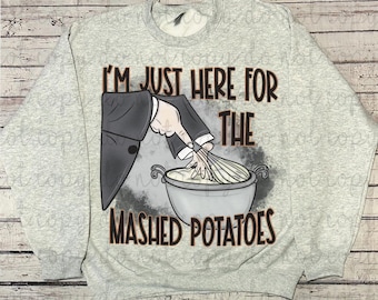 Könnte beinhalten: Hellgraues Sweatshirt mit dem Text "I'M JUST HERE FOR THE MASHED POTATOES" in braunen Buchstaben. Die Grafik zeigt eine Hand im Anzug, die Kartoffelpüree in einer Schüssel mit einem Schneebesen verrührt.