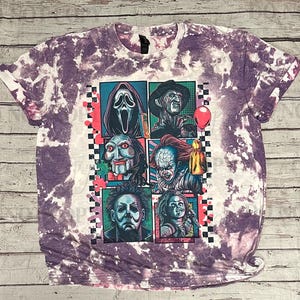 K&ouml;nnte beinhalten: Lila und wei&szlig;es Batik-T-Shirt mit einer Grafik von Horrorfilmfiguren. Die Grafik zeigt Scream, Freddy Krueger, Jigsaw, Pennywise, Michael Myers und Chucky. Das Shirt hat einen Rundhalsausschnitt und umgeschlagene &Auml;rmel.