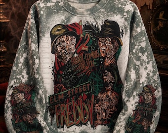 Könnte beinhalten: Ein grau-weißes, säuregewaschenes Sweatshirt mit einem Grafikdruck von Freddy Krueger. Das Design enthält den Text "1, 2 Freddy's coming for you" und "Elm Street Freddy" in roter und grüner Schrift, wiederholt auf den Ärmeln und der Brust.