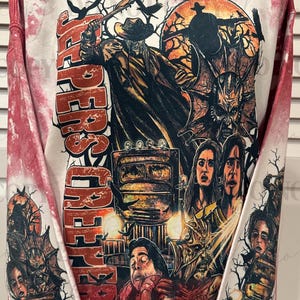 May include: Red and white tie-dye sweatshirt featuring a graphic from the movie Jeepers Creepers. The design includes a figure in a hat, a truck, and the text "Jeepers Creepers" and "What's Eating". The sweatshirt has long sleeves.