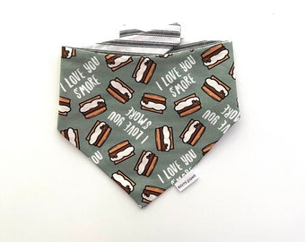 Puede incluir: Bandana verde con ribete blanco y negro a rayas. La bandana tiene un patrón de s'mores marrones y blancos con el texto "I love you s'more" repetido en todo.