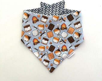 May include: A blue bandana with a pattern of cartoon marshmallows, graham crackers, chocolate squares, and campfires. The bandana has a herringbone pattern on the reverse side and a "Komi Paws" label.