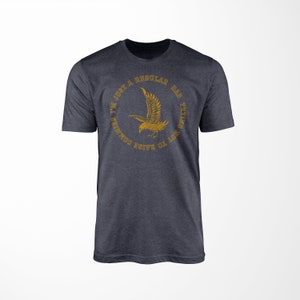 May include: A dark heather grey t-shirt with a gold eagle graphic and the text "I'm just a regular dad trying not to raise communists".