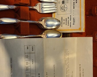May include: A set of silver flatware in a red velvet case. The flatware includes forks, spoons, and knives. The case has a label that says "Tudor Plate by Oneida Community Silversmiths".