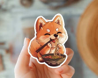 May include: A sticker featuring a cartoon Shiba Inu dog eating ramen noodles with chopsticks. The dog is orange and white with a happy expression. The ramen bowl is blue and white with a design on the side.