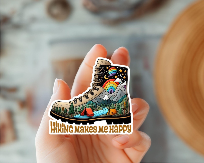 Op de afbeelding: Een kleurrijke sticker met een wandelschoen gevuld met een berglandschap, een regenboog en sterren. De tekst "Hiking Makes Me Happy" staat onder de schoen.