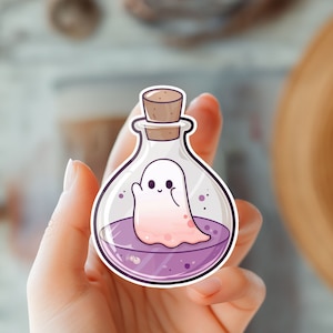May include: A clear glass bottle with a cork stopper filled with purple liquid and a white ghost inside. The bottle has a pink and purple gradient.