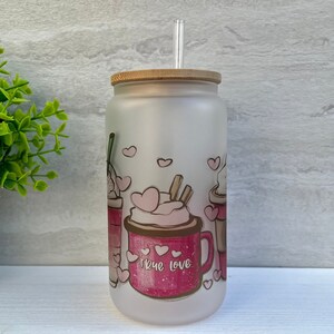 May include: A frosted glass tumbler with a bamboo lid and a clear straw. The tumbler has a pink and brown design of three coffee cups with whipped cream and hearts. The text "True Love" is printed on the front of the tumbler.