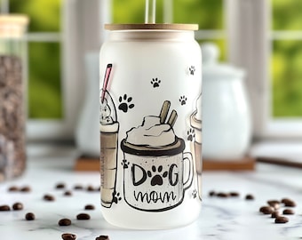 Può includere: Un bicchiere di vetro bianco smerigliato con un coperchio in bambù e una cannuccia. Il bicchiere ha un design con impronte di zampa e il testo "Dog Mom" con un'impronta di zampa nella "O".