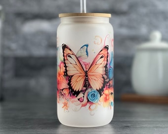 May include: A frosted glass tumbler with a bamboo lid and a straw. The tumbler features a colorful butterfly design with flowers and swirls.