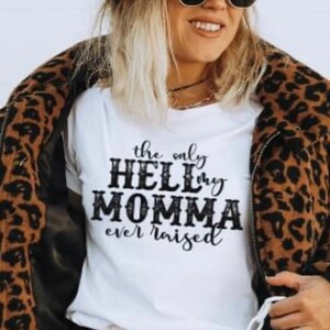 May include: White t-shirt with black text that reads "the only HELL my MOMMA ever raised". The person is wearing a brown leopard print jacket and a brown belt.
