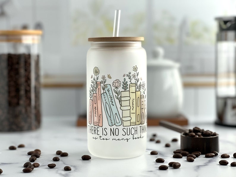 Iced coffee glass can with a graphic containing books and minimalist flowers in pastel colors. The saying there is no such thing as too many books underneath.