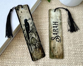 Puede incluir: Dos marcapáginas rectangulares con borlas negras. El de la izquierda muestra un cuervo negro sobre una rama con texto vintage y un reloj. El de la derecha tiene un fondo beige desgastado con el nombre SARAH impreso en color negro.