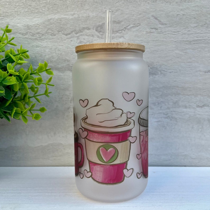 May include: A frosted glass tumbler with a bamboo lid and a clear drinking straw. The tumbler features a pink and white design of coffee cups with hearts and whipped cream.