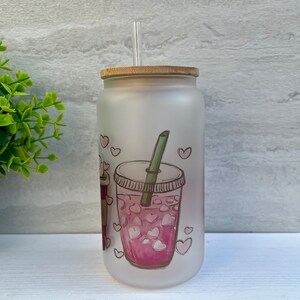May include: A frosted glass tumbler with a bamboo lid and a straw. The tumbler has a pink and white graphic of a cup of iced tea with hearts.