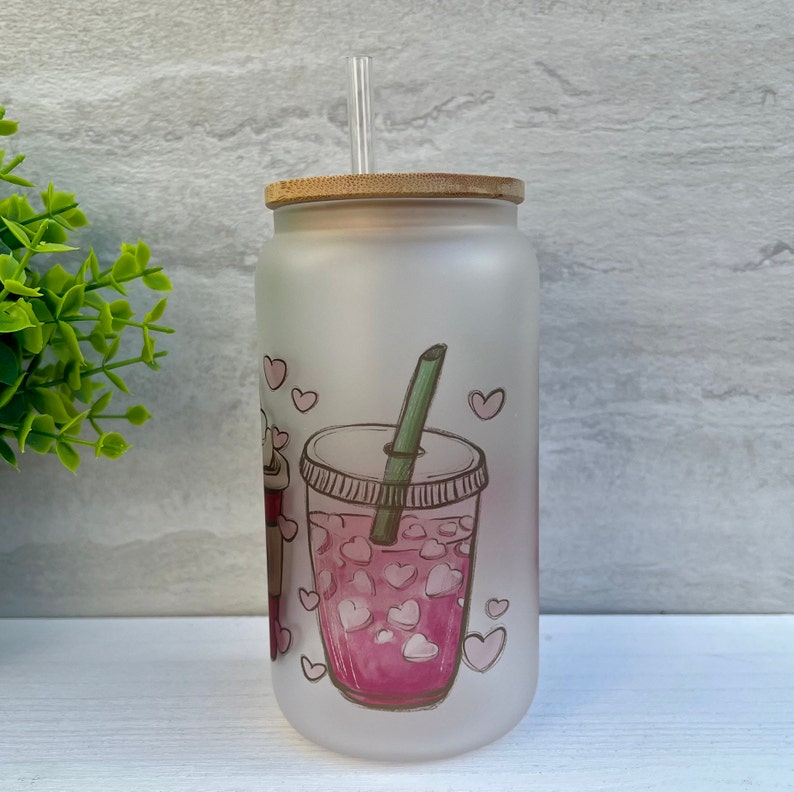 May include: A frosted glass tumbler with a bamboo lid and a straw. The tumbler has a pink and white graphic of a cup of iced tea with hearts.