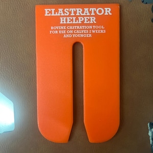 Puede incluir: Herramienta auxiliar Elastrator de plástico naranja brillante. La herramienta tiene un diseño en forma de U con el texto "Elastrator Helper" y "Herramienta de castración bovina para usar en terneros de 2 semanas y menores."