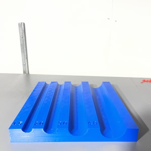 May include: A bright blue, rectangular tool with four curved grooves. The tool has measurements of 15, 20, 30, and 40, likely indicating size or capacity. The object is made of a solid, possibly plastic, material.