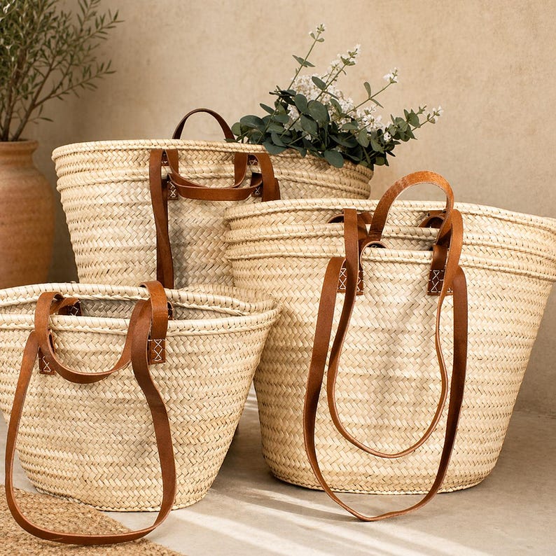 Pu&ograve; includere: Una collezione di borse tote in paglia intrecciata di varie dimensioni. Ogni borsa presenta manici e dettagli in pelle marrone. Le borse sono disposte insieme, alcune contengono vegetazione, suggerendo un'estetica naturale e rustica.