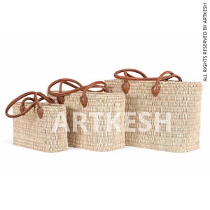 May include: Three woven straw tote bags of varying sizes, each with brown leather handles and accents. The bags are rectangular with rounded corners and are arranged in a row, showcasing their different dimensions. The bags are empty.