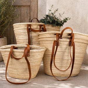 Pu&ograve; includere: Una collezione di cesti in paglia intrecciata di varie dimensioni, ciascuno con manici in pelle marrone. I cesti hanno un colore naturale, marrone chiaro e sono disposti insieme. Alcuni cesti contengono vegetazione.