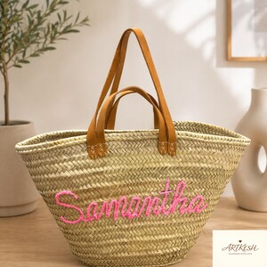 Pu&ograve; includere: Borsa tote in paglia intrecciata con manici in pelle marrone e il nome "Samantha" ricamato in rosa. La borsa ha un design ampio e aperto, adatta per trasportare vari oggetti.