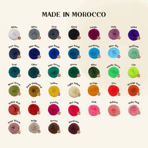 Pu&ograve; includere: Una tabella colori di gomitoli di filato in vari colori, tra cui bianco, nero, viola e verde. Il testo "MADE IN MOROCCO" &egrave; in alto. Ogni colore &egrave; etichettato con un nome e un numero.