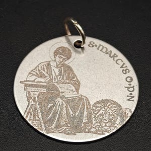 Op de afbeelding: Zilverkleurige ronde hanger met een gedetailleerde gravure van een zittende figuur die aan een bureau schrijft, vergezeld van een leeuw. De tekst "S. IDARCV S. O.P.N" is rondom gegraveerd.