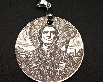 Puede incluir: Un colgante plateado con una imagen grabada de San Patricio sosteniendo un báculo. El colgante circular tiene la inscripción "St. Patrick" en la parte inferior. El fondo es negro.