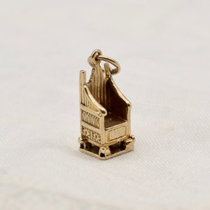 May include: A miniature gold-coloured chair charm with detailed design. The small throne has a high back and a rectangular seat, suggesting a royal theme. The charm is suspended from a small loop, ready to be added to a necklace or bracelet.