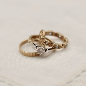 May include: Two gold rings with a diamond on one ring. The rings are on a white lace background.