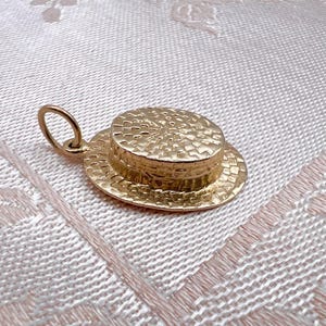 May include: A gold charm in the shape of a straw hat. The hat has a woven texture and a flat brim.