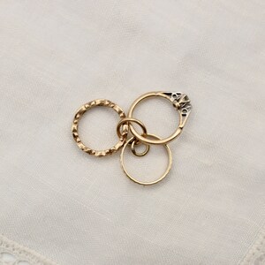 May include: Three gold rings, one with a small diamond, are linked together on a white background.