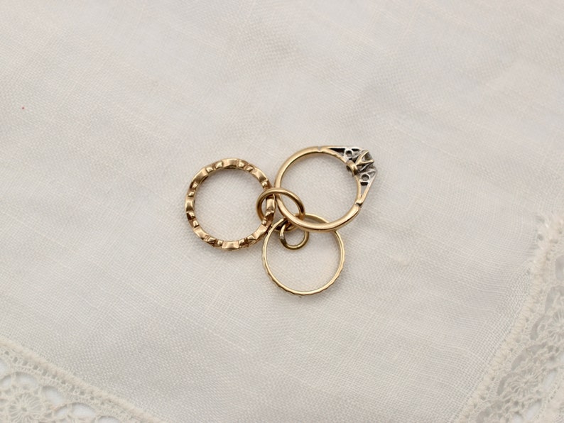 May include: Three gold rings, one with a small diamond, are linked together on a white background.