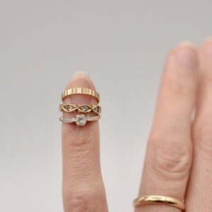May include: A finger wearing four gold rings, including a diamond engagement ring.