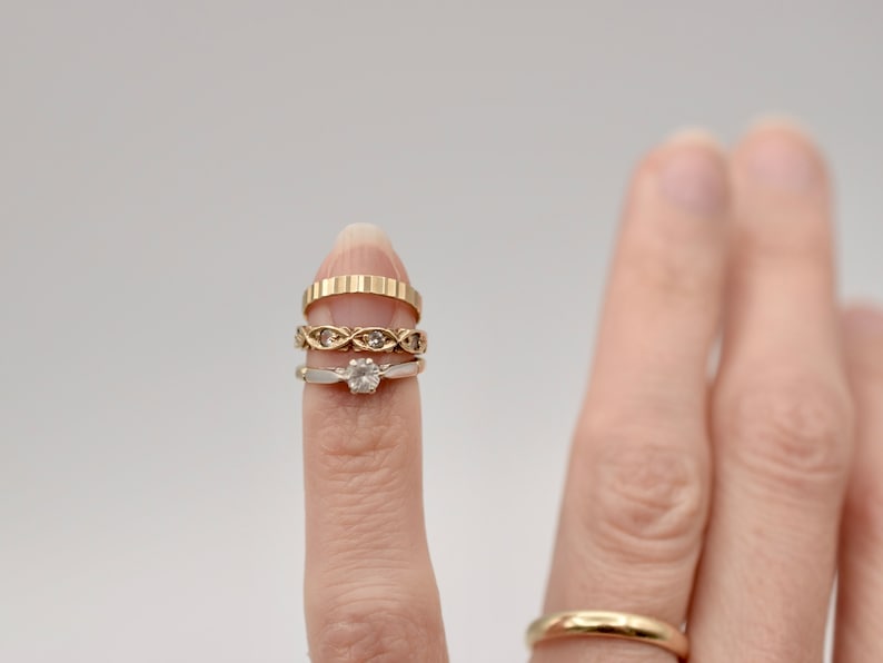 May include: A finger wearing four gold rings, including a diamond engagement ring.