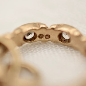 May include: Close-up of the underside of a gold ring with two small clear stones set into the band.
