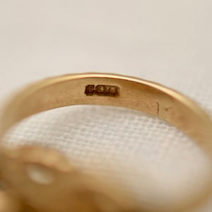 May include: Close-up of the inside of a gold ring with the inscription "925" stamped on the band.
