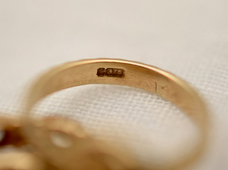 May include: Close-up of the inside of a gold ring with the inscription "925" stamped on the band.