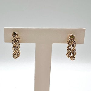 May include: A pair of gold-toned rope-style earrings. The earrings are on a white display stand.