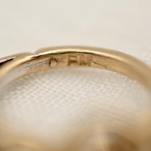 May include: Close-up of the inside of a gold ring with the inscription "FM" on the band.