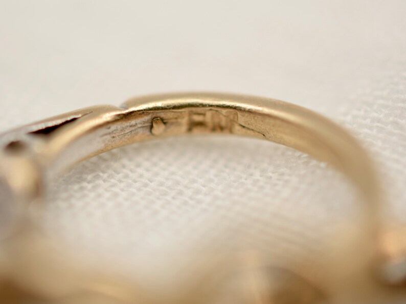 May include: Close-up of the inside of a gold ring with the inscription "FM" on the band.