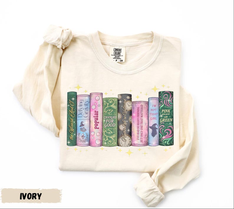 A white long-sleeved t-shirt with a graphic design of a row of colorful books with various titles and illustrations.