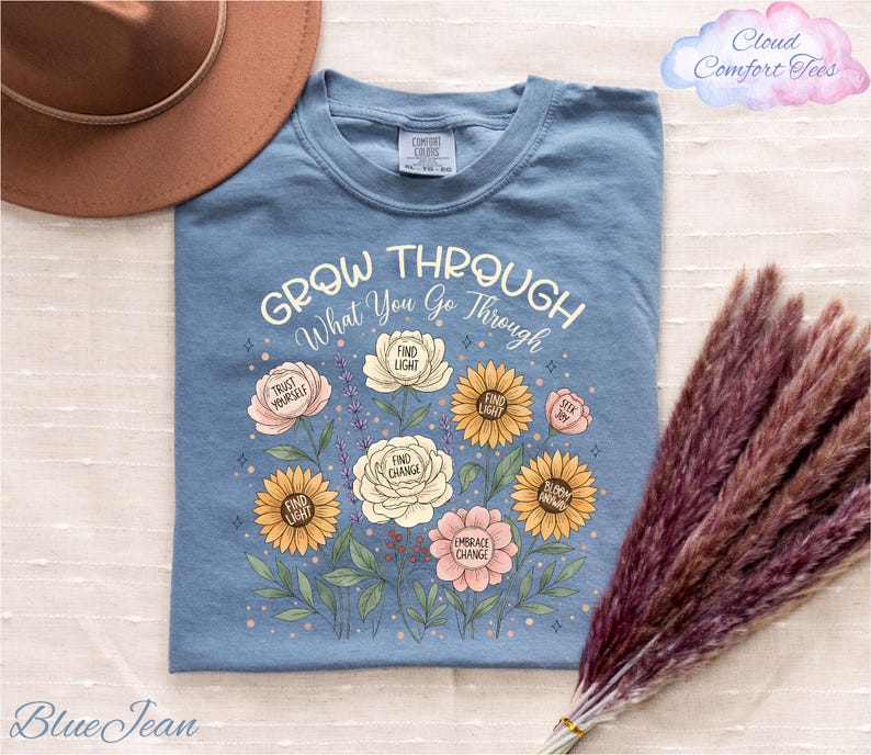 A blue t-shirt with a floral design and the text "Grow Through What You Go Through" printed on it, along with a brown hat and a bunch of purple flowers.