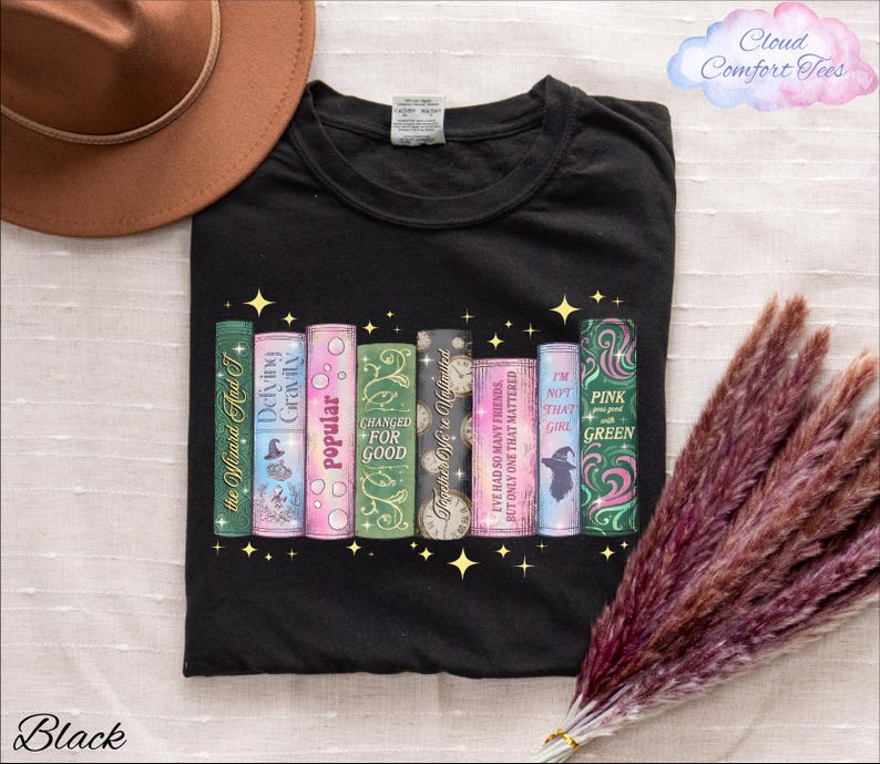 A black t-shirt with a graphic design of colorful books and a brown hat, along with some purple and green decorative elements, and a bunch of purple and green decorative elements.