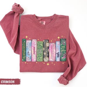 A red long-sleeved t-shirt with a graphic design of a row of colorful books with stars on the cover.